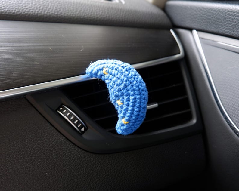 Puede incluir: Un difusor de ventilaci&oacute;n de coche con forma de media luna azul de ganchillo con detalles de estrellas amarillas. El accesorio hecho a mano se coloca en la ventilaci&oacute;n del coche, a&ntilde;adiendo un toque decorativo al interior del veh&iacute;culo.