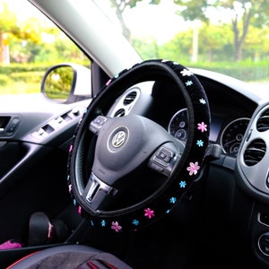 May include: Black steering wheel cover with pink and blue floral embroidery. The cover is made of soft, plush material and fits snugly over the steering wheel.