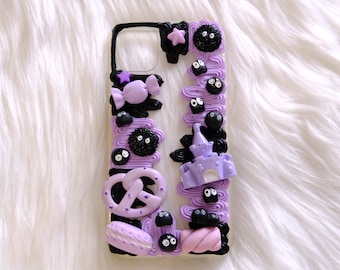 May include: A purple and black phone case with a variety of 3D decorations, including a pretzel, a castle, and a sweet. The decorations are in a whimsical style and are reminiscent of a cartoon.