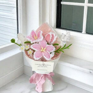 May include: A bouquet of handmade pink crochet flowers with white trim and yellow centers, wrapped in white paper and tied with a pink ribbon. A small card reads "I bought flowers thinking about you..." and "May your days be filled with flowers."