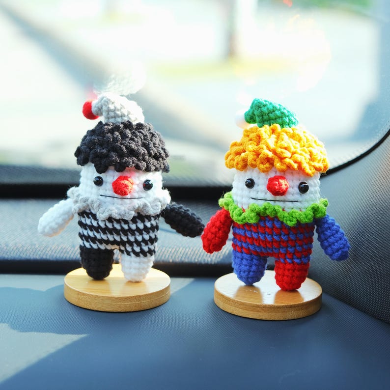 May include: Two handmade crochet clown figurines. One clown has a black and white outfit, the other has a colorful outfit. Both clowns have a red nose, white face, and are mounted on small wooden bases. The clowns have a whimsical design.