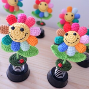 May include: A collection of colorful crocheted flower decorations with smiling faces. Each flower is attached to a spring base and has a small ladybug on the stem.