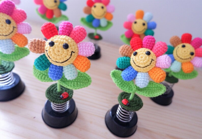 May include: A collection of colorful crocheted flower decorations with smiling faces. Each flower is attached to a spring base and has a small ladybug on the stem.