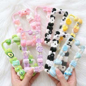 May include: Several decorative phone cases in shades of pink, green, black, and blue. Each case is adorned with unique designs, including sweets, hearts, and other small decorative elements. The cases are held by hands.