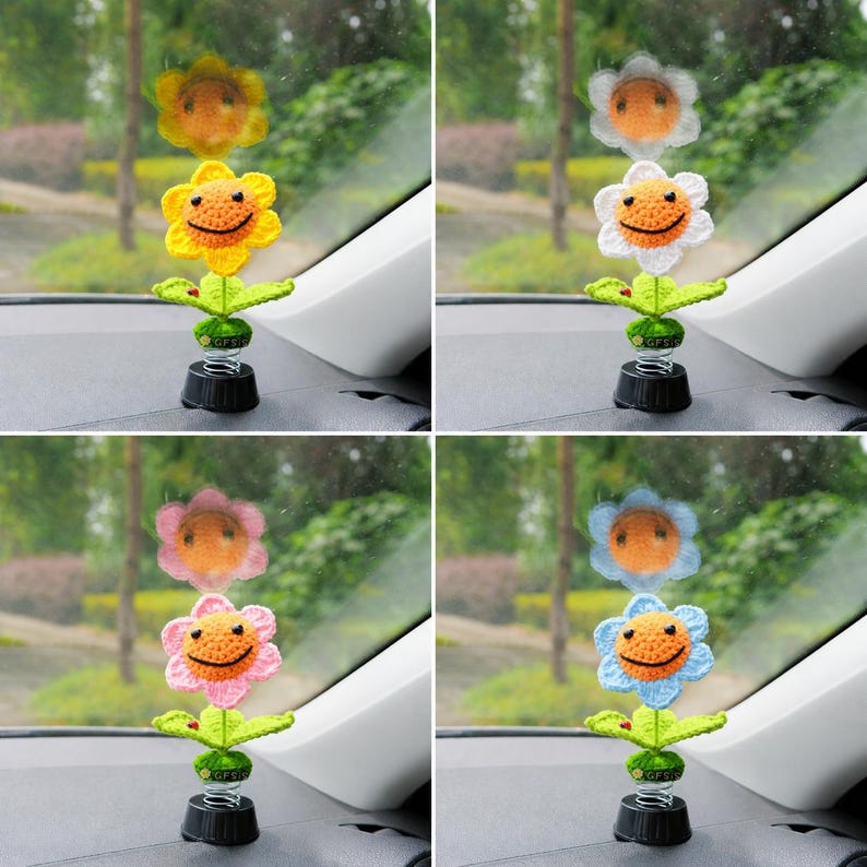 May include: Four car dashboard ornaments. Each features a crocheted flower in yellow, white, pink, or blue, with a smiling face and green leaves. They are mounted on a black base with a spring.