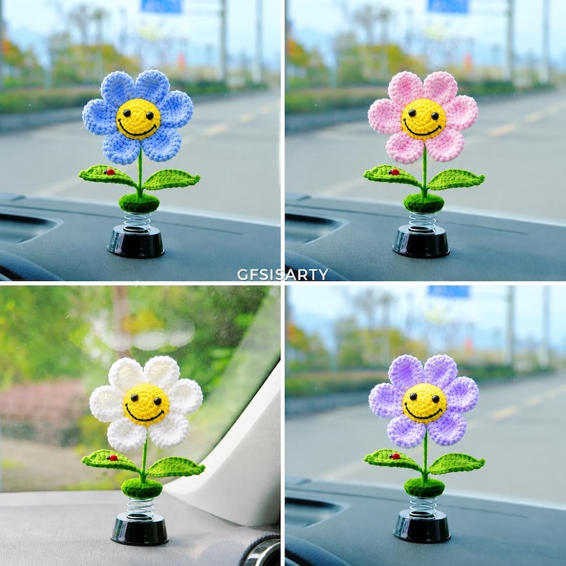 May include: Four crochet flower car decorations in blue, pink, white, and purple. Each flower has a yellow smiley face centre, green leaves, and a black spring base. The text "GFISISARTY" is visible.