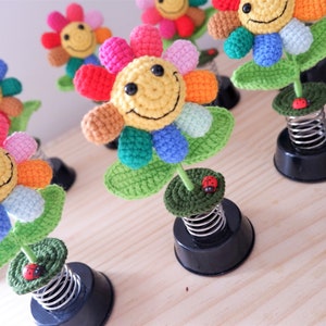 May include: A set of five colorful crocheted flower decorations with smiling faces. Each flower is attached to a spring base and has a small red ladybug on the stem.
