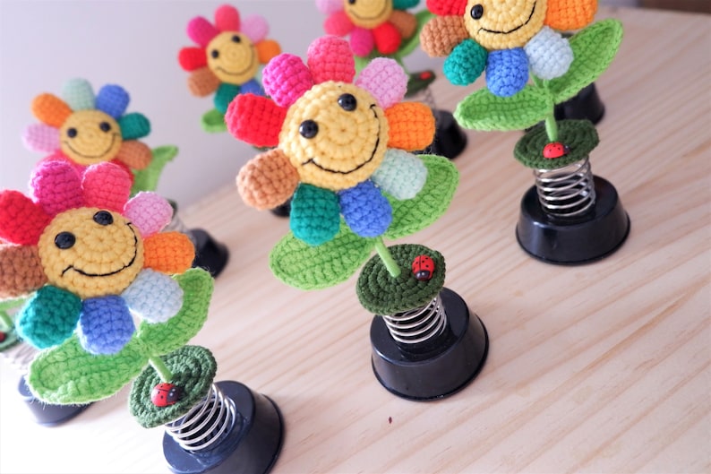 May include: A set of five colorful crocheted flower decorations with smiling faces. Each flower is attached to a spring base and has a small red ladybug on the stem.