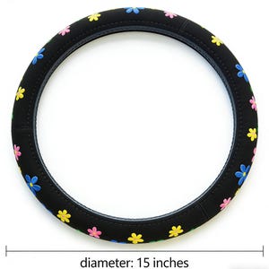 May include: Black steering wheel cover decorated with multi-coloured flower designs. The cover has a diameter of 38 cm. The flowers are yellow, pink, and blue, providing a bright and cheerful look for the car's interior.