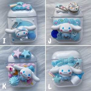 May include: Four clear plastic AirPod cases decorated with pastel blue, pink, and white 3D embellishments. Each case features a white cartoon dog with blue eyes and a pink nose. The embellishments include stars, bows, sprinkles, and a pacifier.
