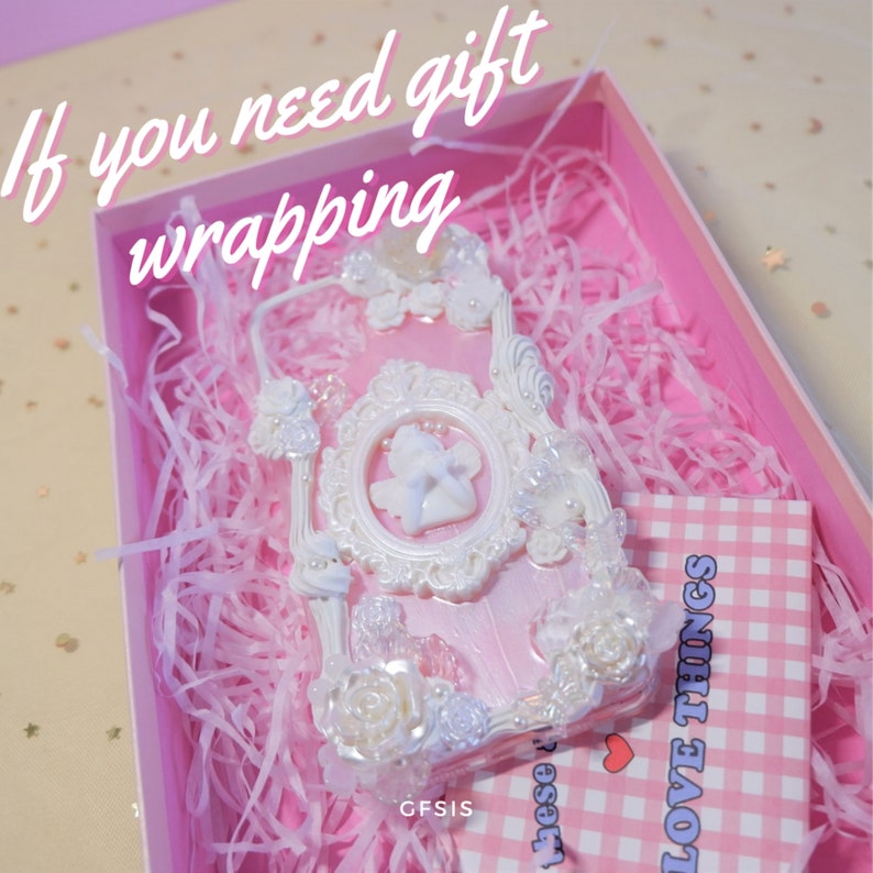 Puede incluir: Una funda de tel&eacute;fono blanca y rosa con un marco decorativo, flores y un dise&ntilde;o de &aacute;ngel. La funda est&aacute; en una caja de regalo rosa con papel de seda rosa. La caja tambi&eacute;n incluye una etiqueta a cuadros rosa y blanca con el texto "LOVE THINGS".