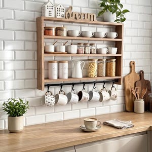 Può includere: Una mensola da parete in legno a quattro livelli, dotata di una barra in metallo nero con sette ganci che sostengono varie tazze in ceramica. I ripiani contengono barattoli di vetro con coperchi in legno, ciotole bianche e una brocca.