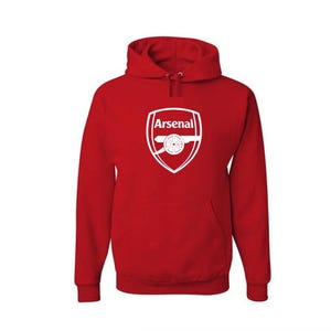 May include: A red hooded sweatshirt featuring the Arsenal logo in white. The logo is a shield shape with the word "Arsenal" above a cannon. The sweatshirt has a front pocket and a drawstring hood.