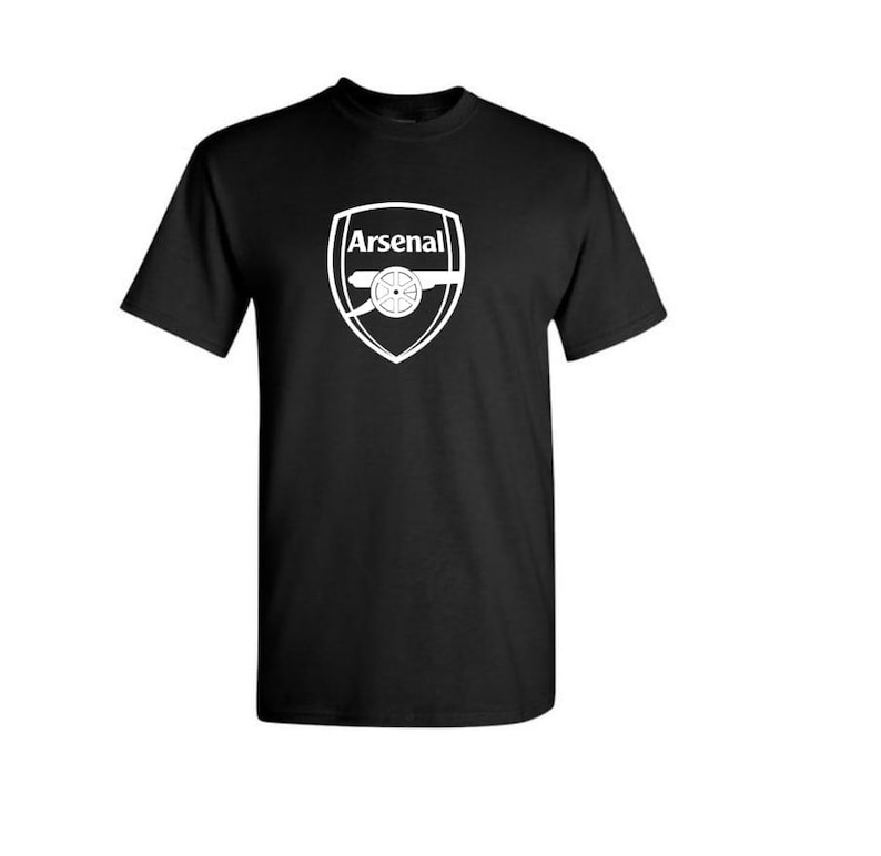 May include: Black t-shirt with the Arsenal logo printed in white. The logo is a shield shape with the word "Arsenal" above a cannon. The shirt has a crew neck and short sleeves.