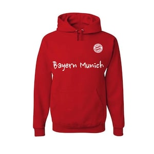 May include: A red hooded sweatshirt with the words "Bayern Munich" in white script across the chest. The sweatshirt has a front pocket and a small emblem on the upper right chest.