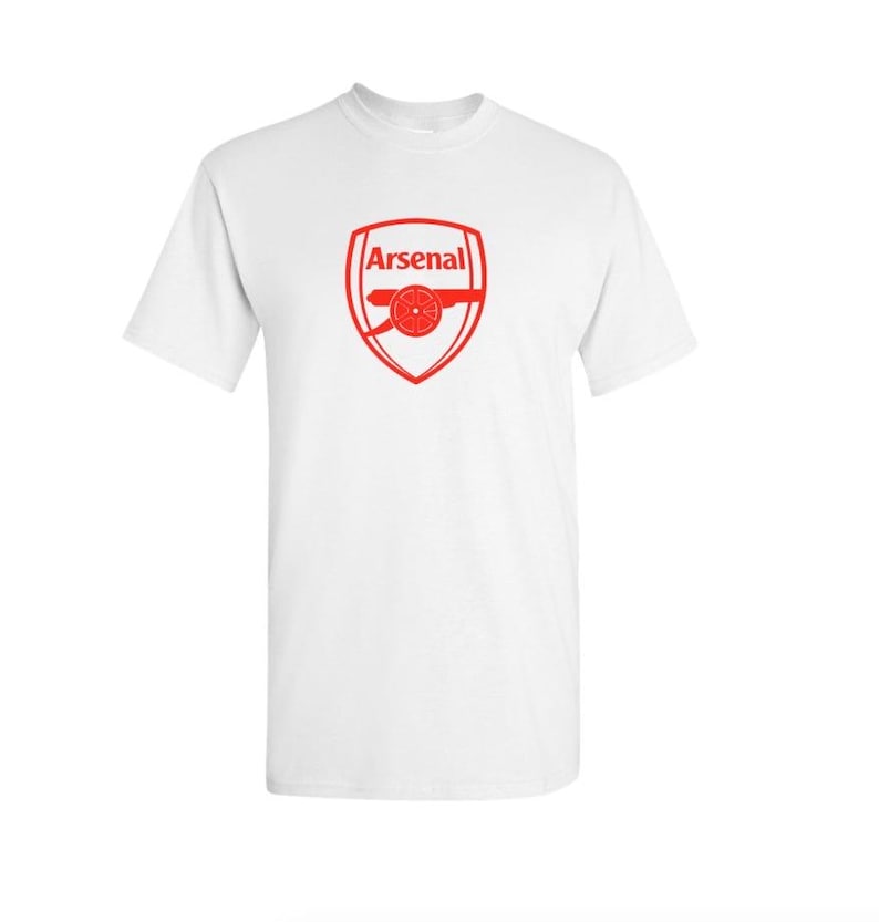 May include: White t-shirt with the red Arsenal logo. The logo features the word "Arsenal" above a cannon design inside a shield. The shirt has a crew neck and short sleeves.