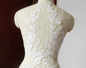 May include: White lace applique with floral designs. The lace is delicate and intricate, with a variety of flower shapes and sizes. The applique is perfect for adding a touch of elegance to any garment.