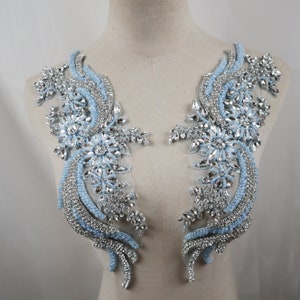 May include: A pair of light blue and silver beaded appliques with a floral design. The appliques are perfect for adding a touch of sparkle to any garment.