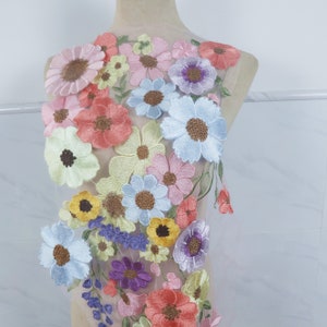 May include: A sheer fabric with embroidered flowers in various colors, including pink, blue, yellow, and purple. The flowers are layered and overlapping, creating a three-dimensional effect.