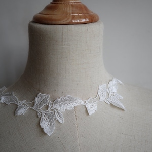 May include: White lace trim with a leaf design. The trim is shown on a white dress form.