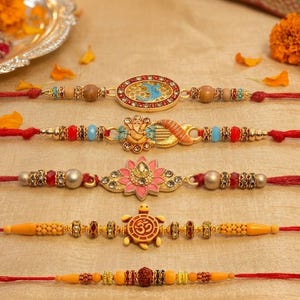 May include: Five decorative bracelets featuring red threads and central ornaments. The designs include an oval blue inlay, a gold-toned Ganesha figure, a pink lotus flower with crystals, a yellow turtle with an Om symbol, and a central brown bead.