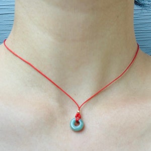 Può includere: Una collana di corda rossa con un ciondolo di giada verde a forma di cerchio.