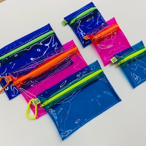 May include: A collection of five rectangular translucent pouches in blue and hot pink. Each pouch features a contrasting neon zipper closure in lime green or orange, and includes a matching plastic carabiner attached to the zipper pull.