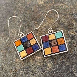 May include: A pair of square earrings with a mosaic tile design. Each earring features a silver frame and a grid of colorful tiles in shades of red, orange, blue, yellow, and turquoise. The earrings have silver hooks.