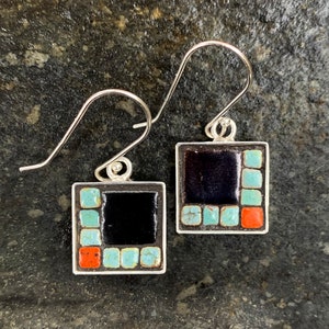 May include: Square silver earrings with a mosaic design. Each earring features a black center square surrounded by turquoise and red tiles. The earrings have silver ear wires.