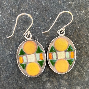 May include: A pair of silver earrings with a geometric design. The earrings are made of small, colorful tiles in shades of yellow, green, orange, and white. The tiles are arranged in a symmetrical pattern.