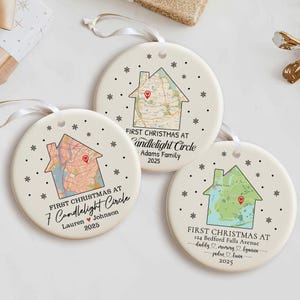 Puede incluir: Tres adornos navideños redondos de cerámica con un diseño de mapa en forma de casa. Cada adorno presenta una dirección y un apellido diferentes, con el texto "First Christmas at" y el año 2025. Cinta blanca para colgar.