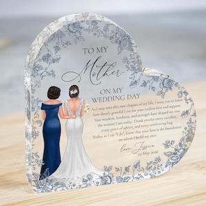 Op de afbeelding: Een hartvormig aandenken van acryl met een bloemenontwerp en de tekst "TO MY Mother ON MY WEDDING DAY". Het bevat illustraties van een bruid en haar moeder. De datum "25 mei 2026" is ook opgenomen.