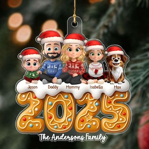May include: A personalized Christmas ornament featuring a family of five and a dog, all wearing Santa hats. The ornament includes the year "2025" and the family name "The Andersons Family" in a gingerbread-style design. The ornament is suspended by a gold string.
