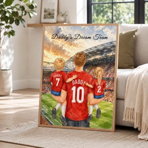 May include: A framed watercolor-style print titled Daddy's Dream Team, depicting a person in a red jersey numbered 10 holding two children in matching red jerseys numbered 7 and 2, standing on a soccer field inside a large stadium at sunset.