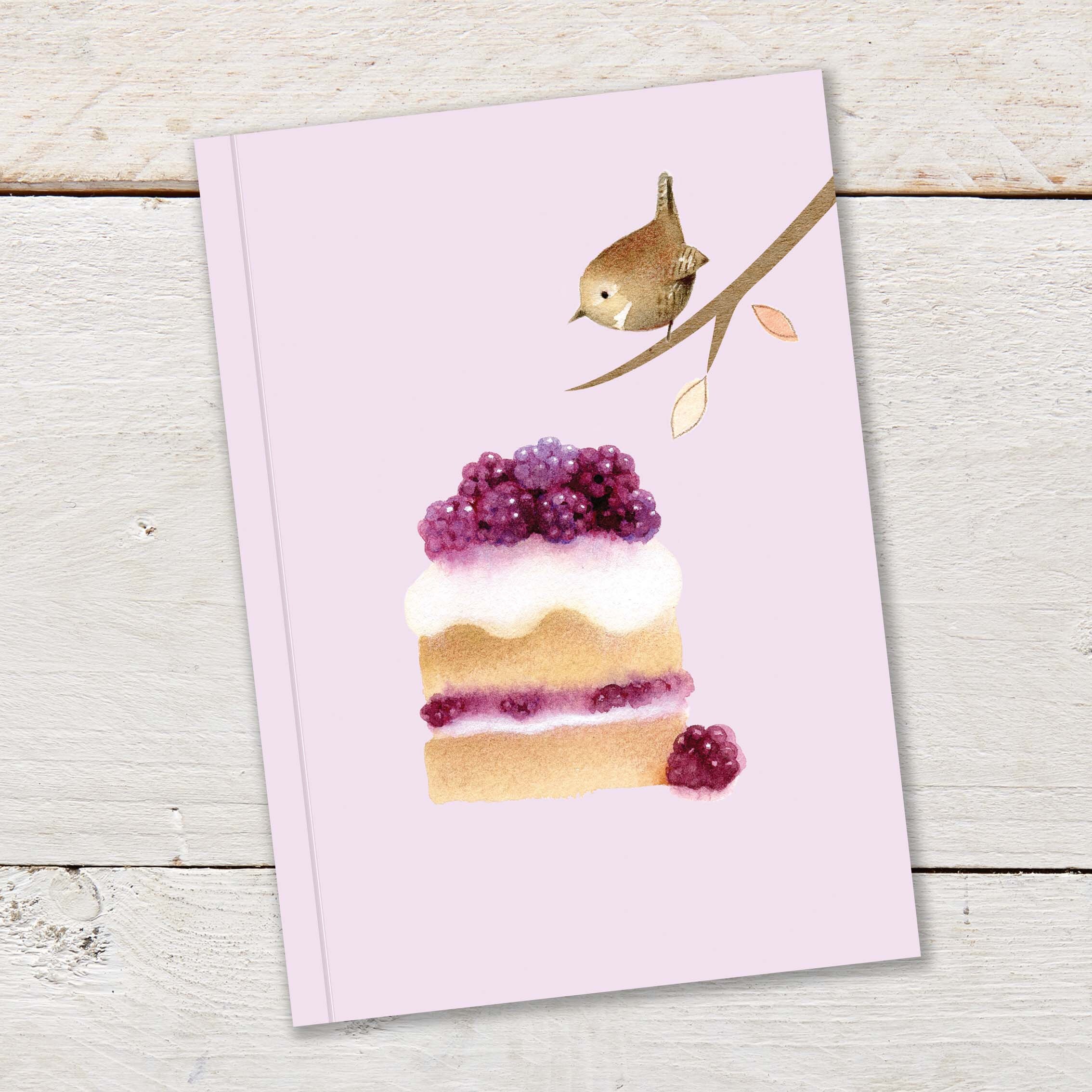 A6 96pp Notebook featuring a cute wren with a large slice of blackberry cake on a pale lilac background colour. Notebook is ruled.