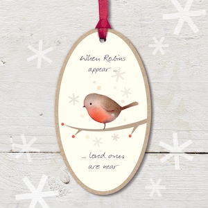 May include: Oval-shaped Christmas ornament with a red ribbon. The ornament features a watercolor illustration of a robin perched on a branch, with the text "When Robins appear... loved ones are near."