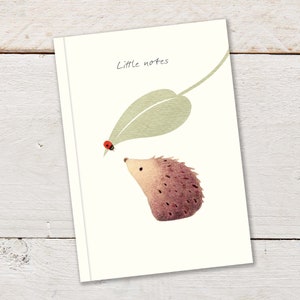 A6 96pp Notizbuch mit niedlichem Marienkäfer und Igel auf einem großen Blatt, auf cremefarbener Hintergrundfarbe und mit der Überschrift ""Little Notes""." Notebook ist liniert.