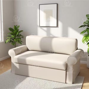 Puede incluir: Un sofá de dos plazas color crema con brazos enrollados y una base con falda. El sofá está colocado sobre una alfombra de color claro, con dos plantas verdes a cada lado. Una imagen enmarcada cuelga de la pared detrás del sofá.