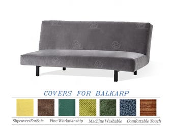 May include: A grey futon sofa with black legs. The sofa has a low profile and a simple design. Below the sofa, there is text that reads "COVERS FOR BALKARP" and a colour swatch selection of slipcovers.