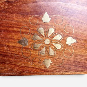 May include: A set of semi-circular wooden coasters featuring a rich brown grain and a central brass inlay. The inlay depicts a stylized flower with twelve petals surrounded by four leaf-shaped accents and thin, curved decorative lines.