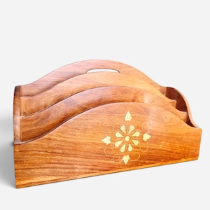 May include: A wooden letter holder featuring three tiered compartments with wavy edges. The front panel is decorated with a central brass inlay depicting a stylized flower surrounded by delicate swirling lines and small leaf-shaped accents.