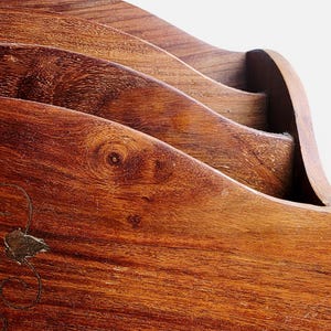 May include: A wooden letter holder featuring a tiered, wave-like design with multiple slots for organizing documents. The natural brown wood grain is visible throughout, and a small, metallic floral inlay is embedded on the front panel.