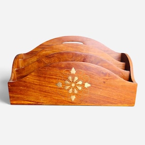 May include: A brown wooden letter holder featuring three tiered compartments with a curved top edge and a central brass inlay depicting a floral motif surrounded by delicate swirling lines, showcasing a natural wood grain finish throughout the piece.
