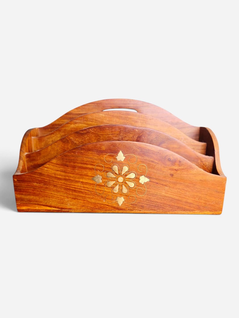 May include: A brown wooden letter holder featuring three tiered compartments with a curved top edge and a central brass inlay depicting a floral motif surrounded by delicate swirling lines, showcasing a natural wood grain finish throughout the piece.