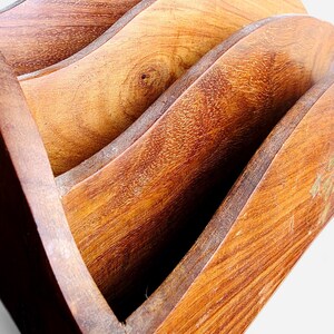May include: A wooden letter holder featuring three curved, tiered compartments with a visible natural wood grain pattern. The structure is crafted from polished brown wood, showcasing distinct knots and textures across the arched dividers.