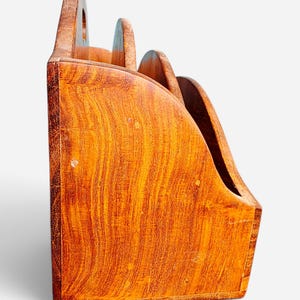 May include: A wooden desk organizer with a natural grain finish, featuring three tiered compartments with curved side panels. The structure is made of light brown wood with visible vertical grain patterns and rounded edges on each divider section.