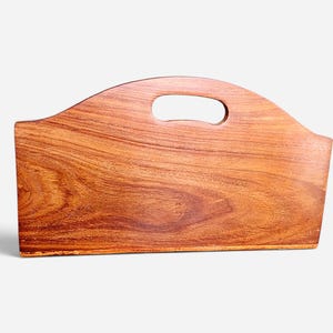 May include: A rectangular wooden magazine rack with a rich, warm brown grain pattern. The top edge features a smooth, arched design with a central oval cutout that serves as a handle for carrying. The structure is solid with a flat base.