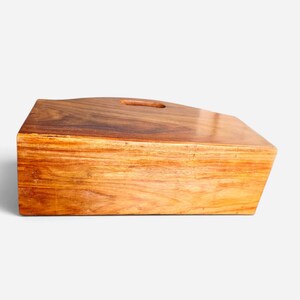 May include: A rectangular wooden serving board with a smooth, polished finish and a rich brown grain pattern. The board features a slightly angled top edge and a single oval-shaped cutout handle positioned near the center of the upper surface.
