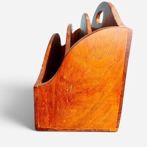 May include: A wooden desk organizer with a warm brown finish and visible wood grain. The organizer features three tiered compartments with curved side panels and a cutout handle at the top, providing a structured space for holding documents or mail.