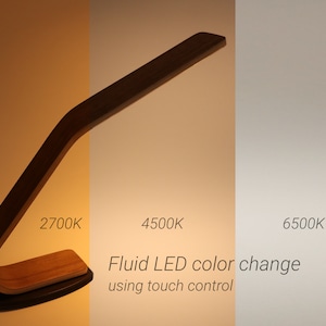 May include: A wooden desk lamp with a curved arm and a touch-sensitive base. The lamp has three different color temperature settings: 2700K, 4500K, and 6500K. The text "Fluid LED color change using touch control" is displayed below the lamp.